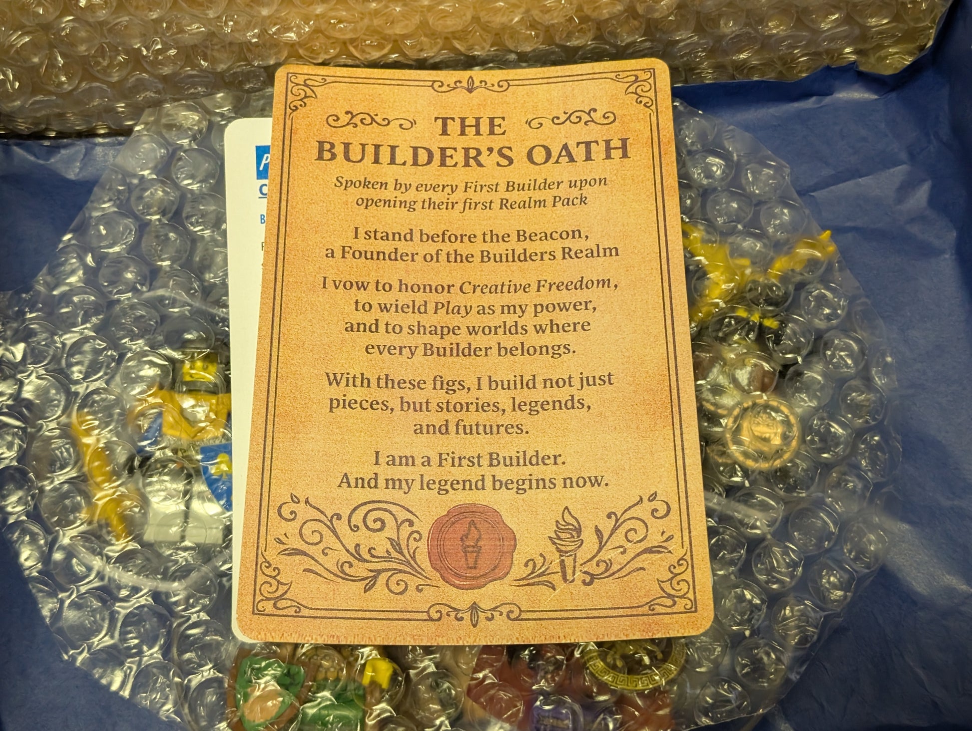Card titled 'The Builder's Oath' on a surface with small figurines and packaging materials.